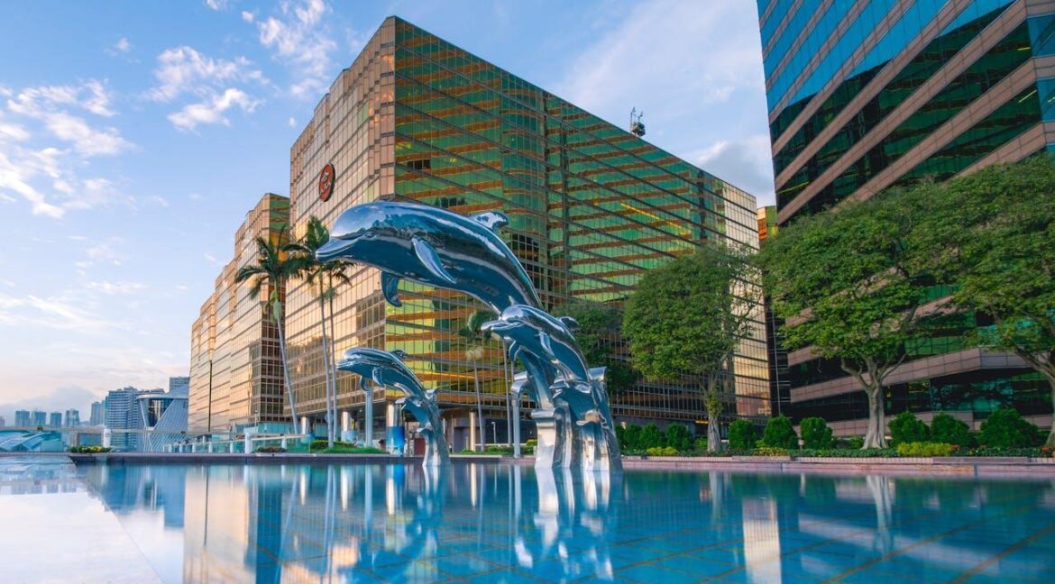 Three blue dolphin statues in a pool of water in front of buildings.