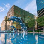 Three blue dolphin statues in a pool of water in front of buildings.