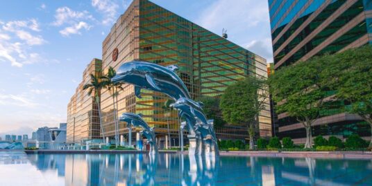 Three blue dolphin statues in a pool of water in front of buildings.